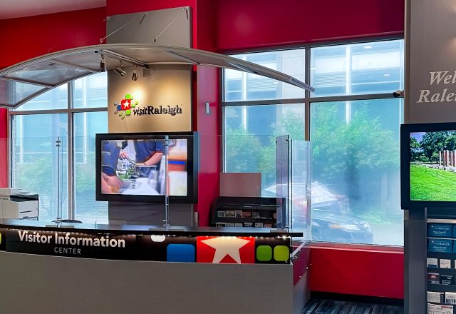 Visitor Information Center in Raleigh showing welcome desk, a colorful interior, digital screens, brochures visitor services area.