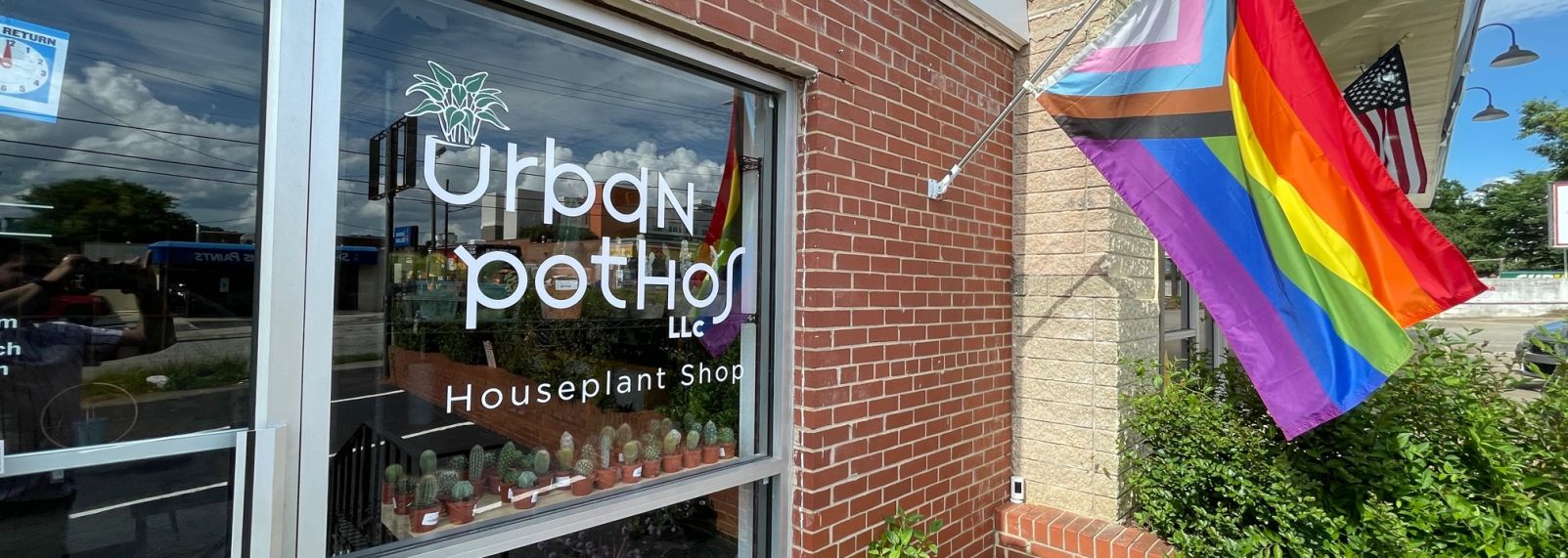 Urban Pothos storefront in Raleigh, rainbow pride flag outside brick building entrance, and houseplant window display greenery.