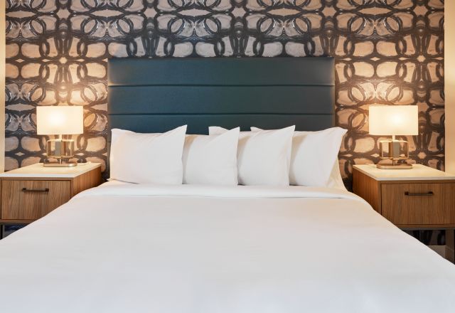 Modern Hive House hotel bedroom in Raleigh, NC, with a king bed, white pillows, stylish headboard, patterned wallpaper, and bedside lamps.