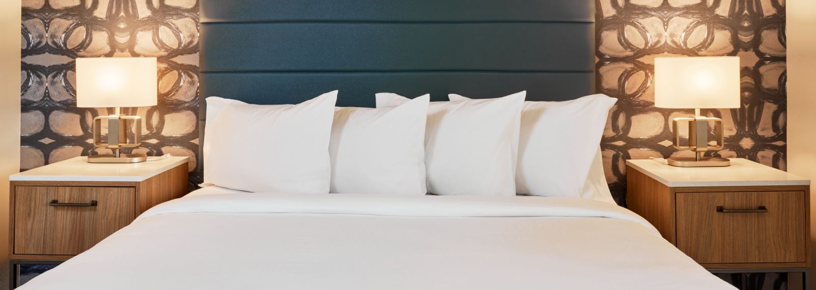 Modern Hive House hotel bedroom in Raleigh, NC, with a king bed, white pillows, stylish headboard, patterned wallpaper, and bedside lamps.